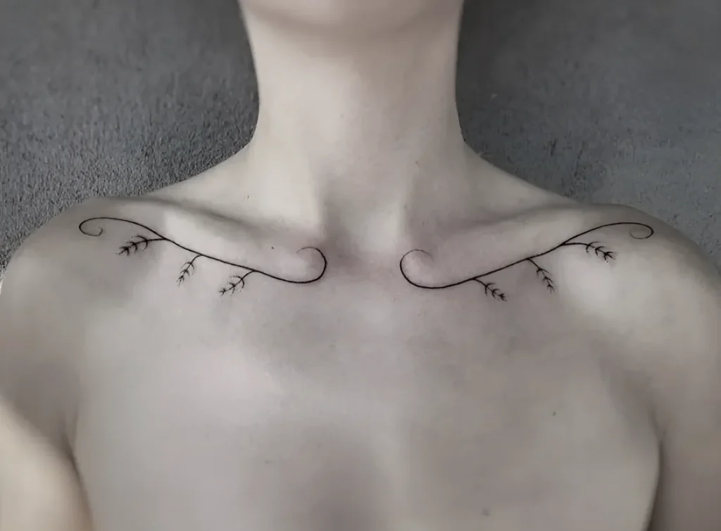 Photo of a collarbone tattoo: black graphic, a thin branch with small flowers, placed along the collarbone bone