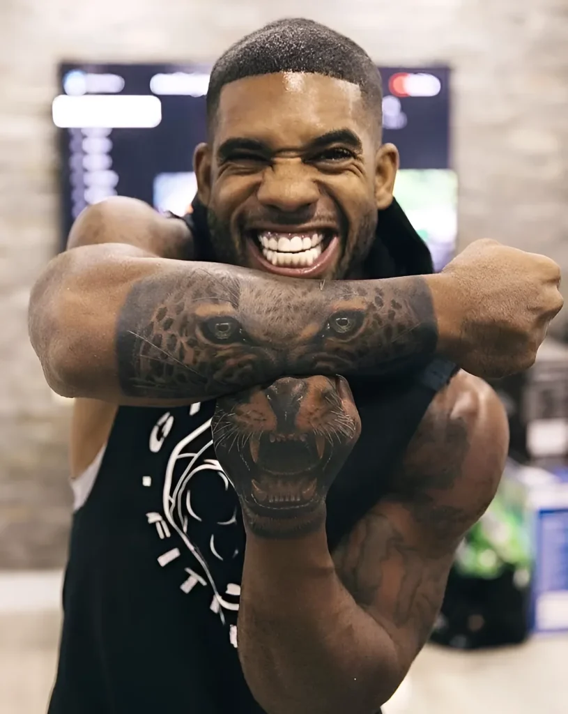 Man displaying a forearm tattoo of a realistic lion's head emerging from a sleeve of dark spots, symbolizing strength and leadership.
