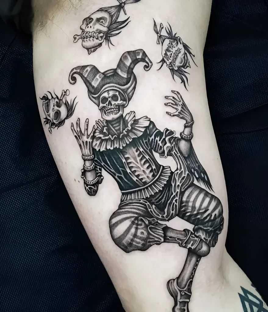 Tatouage noir et blanc sur le biceps : Squelette en costume de bouffon, entouré de crânes flottants, réalisé dans un style Old School.