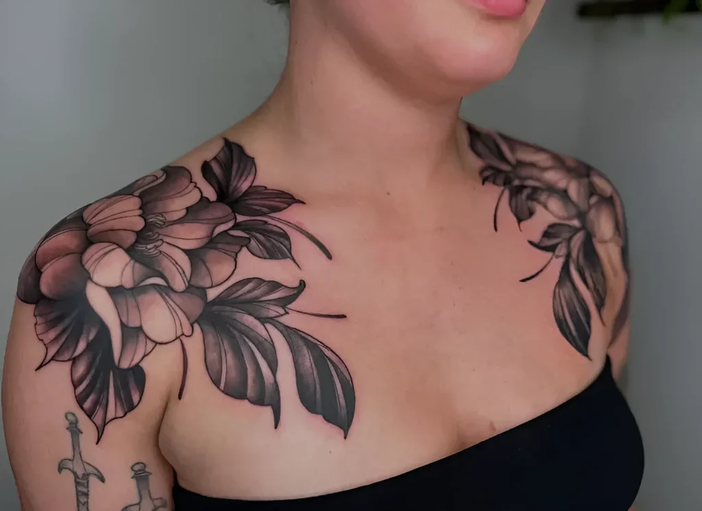 Black and grey peony tattoo on the deltoid muscles, done in realistic style with emphasis on smooth shadow transitions.