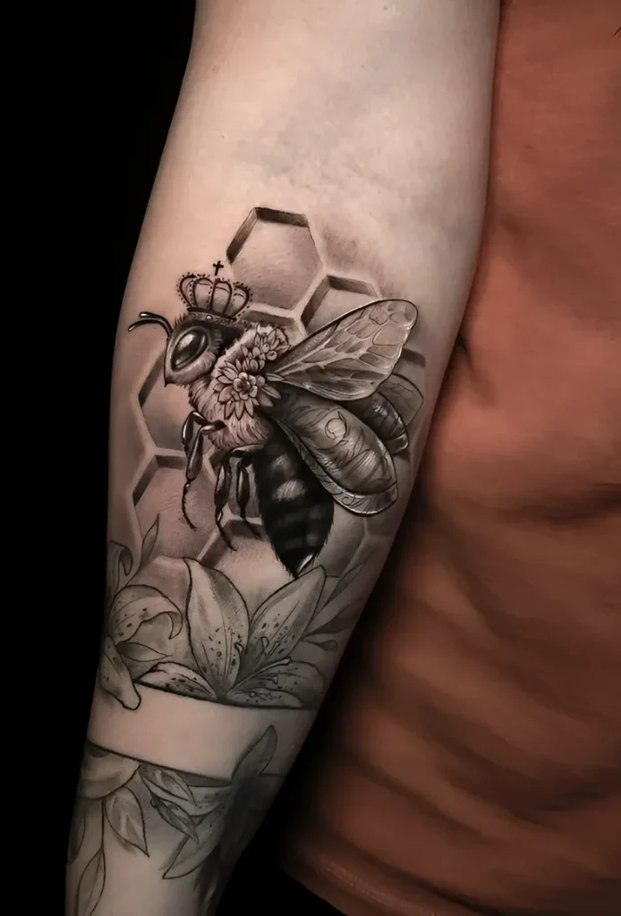 Black and grey realistic tattoo of a bee in a crown on the forearm, surrounded by honeycomb and flowers.