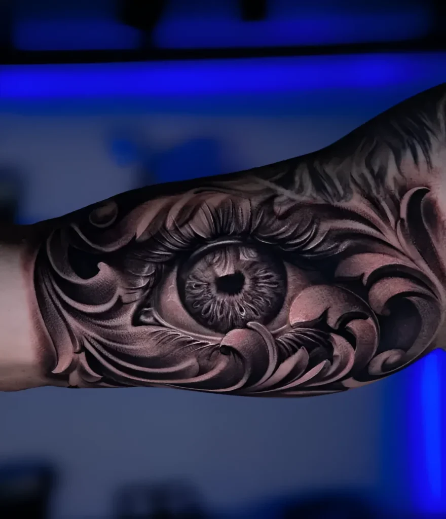 Photo de tatouage sur le biceps : image réaliste d'un œil humain, entouré d'un ornement complexe de style blackwork.
