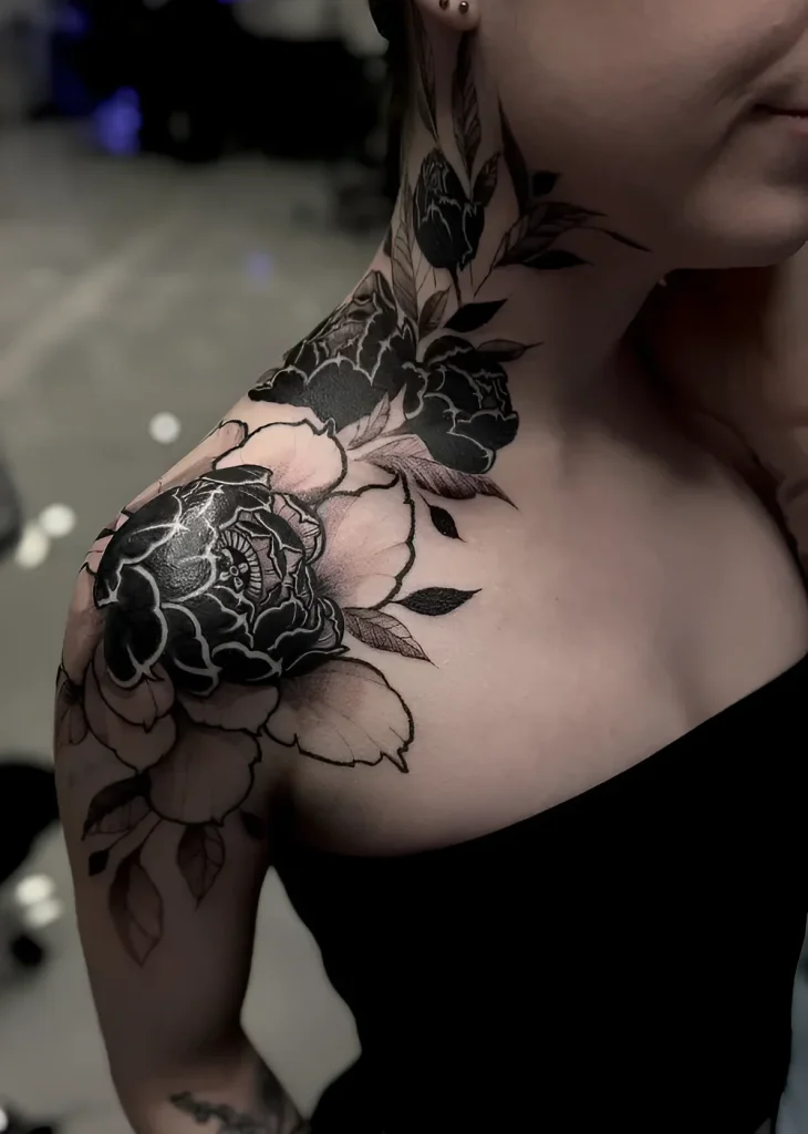 Black and white peony tattoo on the deltoid muscle, done in realistic graphic style.