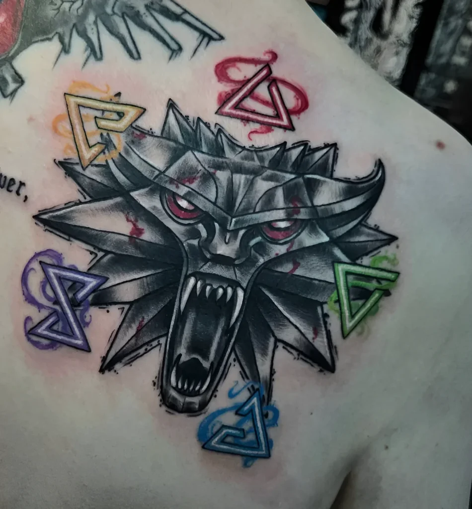 Black and grey tattoo on the shoulder blade: the head of a Witcher surrounded by geometric shapes and paint splashes.
