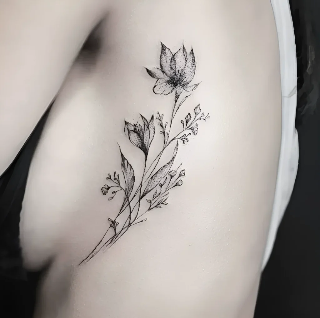 Tatouage noir et blanc d'une branche avec des fleurs sur le flanc de la cage thoracique, réalisé en technique de graphisme fin, photo pour inspiration.