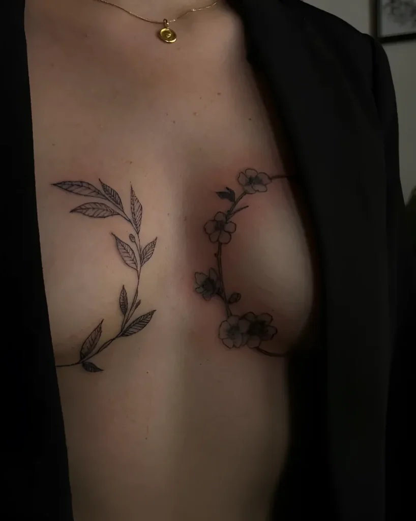 Black and white tattoo under the breast with an image of an olive branch and blooming sakura, done in linework technique, on delicate female skin.