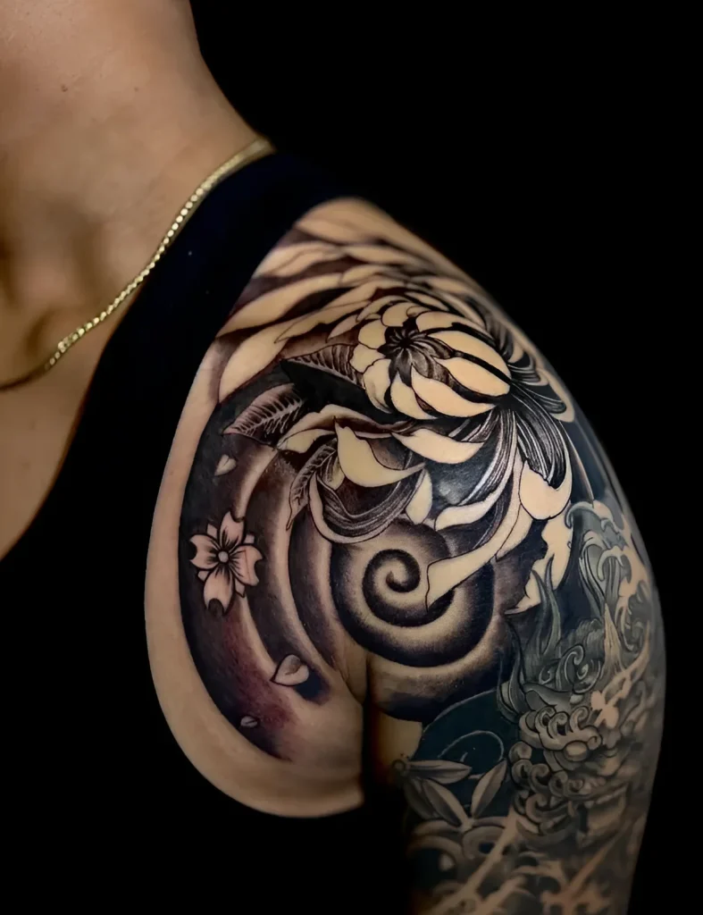 Black and white shoulder tattoo depicting a blooming peony, a wave, and sakura, done in realism.