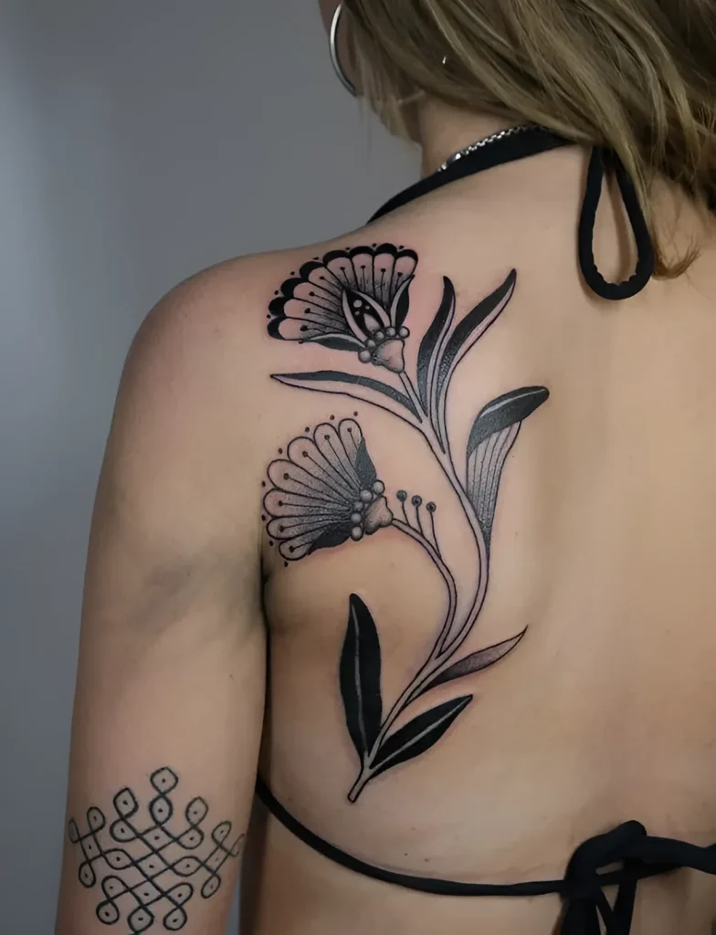 Photo of a tattoo on the shoulder blade: two flowers with detailed petal and stem rendering in graphic technique.