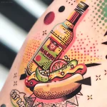 Яркая татуировка хот-дога с бутылкой Malort на руке, выполненная в стиле нео-трад