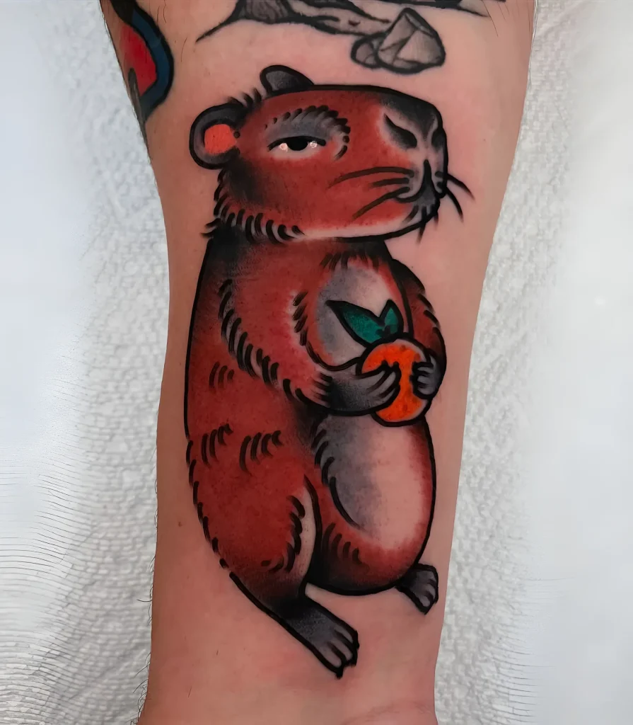 Tatouage coloré d'un capybara tenant une orange, style old school sur le bras