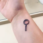 Минималистичная татуировка лупы на запястье в технике blackwork, символизирующая внимательность и стремление к познанию.