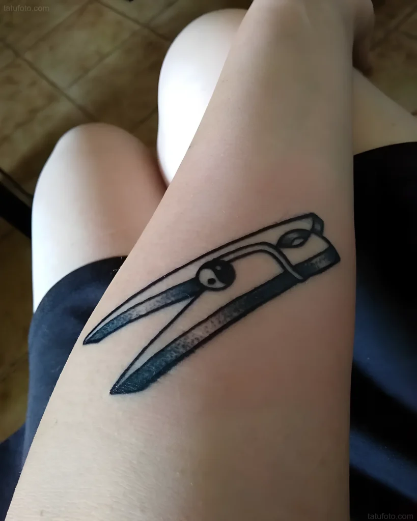 Tatouage en noir et blanc d'une pince à linge sur l'intérieur de la cuisse, réalisé dans un style minimaliste.