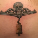 Татуировка штопора с черепом в стиле олд скул, выполненная в приглушенных серых и золотых тонах на коже.