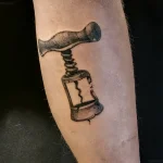 Черно-серая татуировка штопора на ноге, выполненная в реалистичном стиле с детальной проработкой металла и тени.