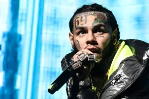 Рэпер 6ix9ine (Даниэль Эрнандес) выступает на сцене в Майами, держа микрофон, с многочисленными татуировками на лице, включая татуировки на лбу.