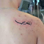 Фото татуировки: Арабская надпись 'المغربية' на лопатке мужчины, выполненная черными чернилами в каллиграфическом стиле.