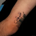 Фотография татуировки надписи «فلسطين» на внутренней стороне предплечья, выполненной четкой каллиграфией.
