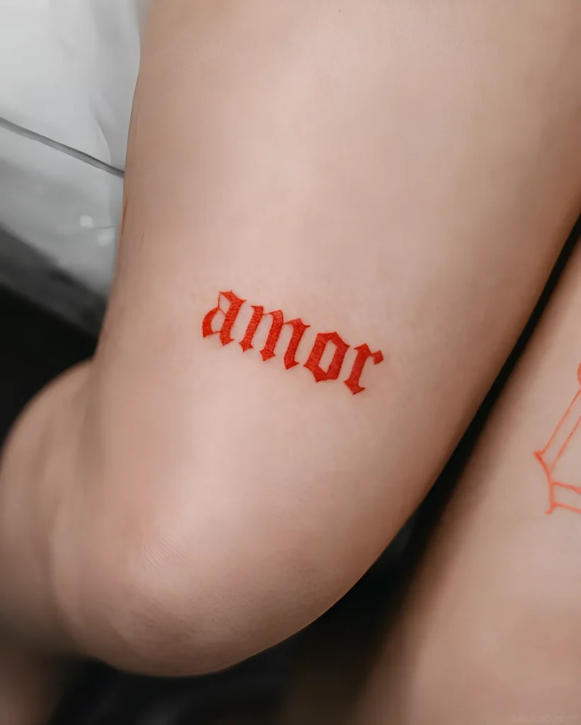 Крупный план татуировки надписи 'amor' на внутренней стороне руки, выполненной в готическом стиле красным цветом.