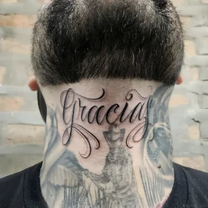 Фото татуировки надписи “Gracia” на затылке, выполненной в черном цвете, с плавными линиями и каллиграфическим шрифтом.