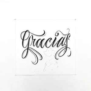 Эскиз татуировки надписи 'Gracias' выполненной в стиле каллиграфии, черные чернила на белом фоне.
