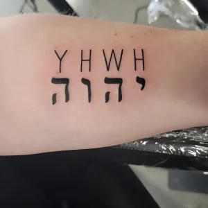 Фотография татуировки на руке: четкое изображение имени Бога на иврите (YHWH) в строгом минималистичном стиле.