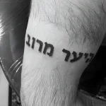 Черно-белая фотография татуировки на руке: ивритская надпись «Леэр мероц» выполненная четким шрифтом.
