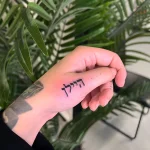 Минималистичная татуировка надписи на иврите «לְהִתְגַּלּוֹת» на запястье, выполненная черными чернилами.