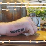 Черно-белая татуировка надписи на иврите на тыльной стороне кисти руки мужчины, четкие линии и традиционный шрифт.