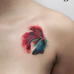 Яркая акварельная татуировка Петушка на ключице, сочетающая красный, синий и бирюзовый цвета.