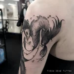 Черно-белая татуировка петушка на плече, выполненная в технике графики с детализированными плавниками и пузырьками воздуха.