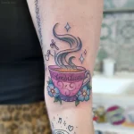Яркая татуировка на ноге: розовая чашка кофе с паром и надписью 'Cup of Ambition', украшенная голубыми цветами.