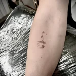 Минималистичная татуировка чашки с паром в виде сердечка на внутренней стороне предплечья