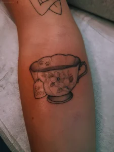 Черно-белая татуировка чашки с белыми цветами и биркой Earl Grey на руке