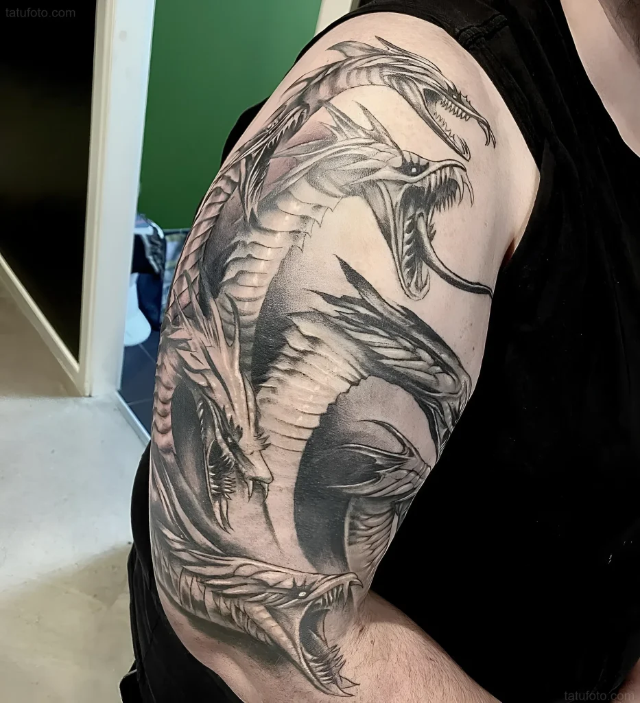 Black and white tattoo of a multi-headed Hydra snake on the bicep, showing an aggressive composition and scale detail