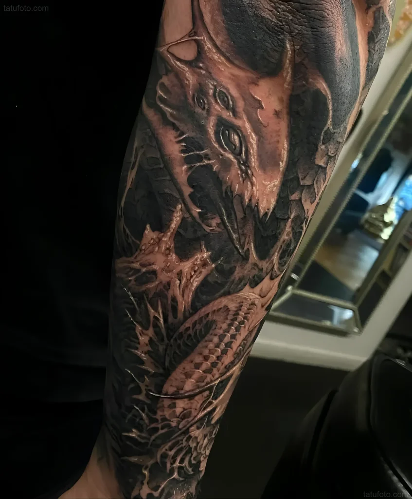 Black and white tattoo of a Hydra in realism style with emphasis on a detailed head and scales on the forearm.