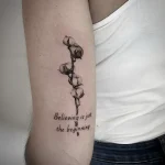 Минималистичная татуировка ветки хлопка с надписью "Believing is just the beginning"
