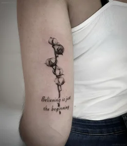 Минималистичная татуировка ветки хлопка с надписью "Believing is just the beginning"