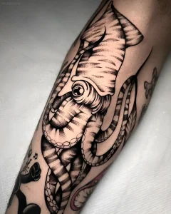 Черно-белая татуировка кальмара на бицепсе, выполненная в технике Blackwork с детализированной проработкой текстур и теней.