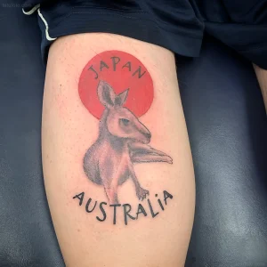 Черно-серая татуировка кенгуру на бедре, с надписями 'JAPAN' и 'AUSTRALIA' в красном круге и под ним.