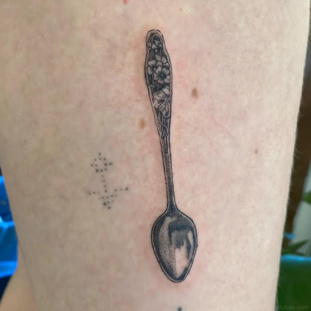 Schwarz-weißes Löffel-Tattoo mit Blumenmuster am Griff, platziert am Bein.