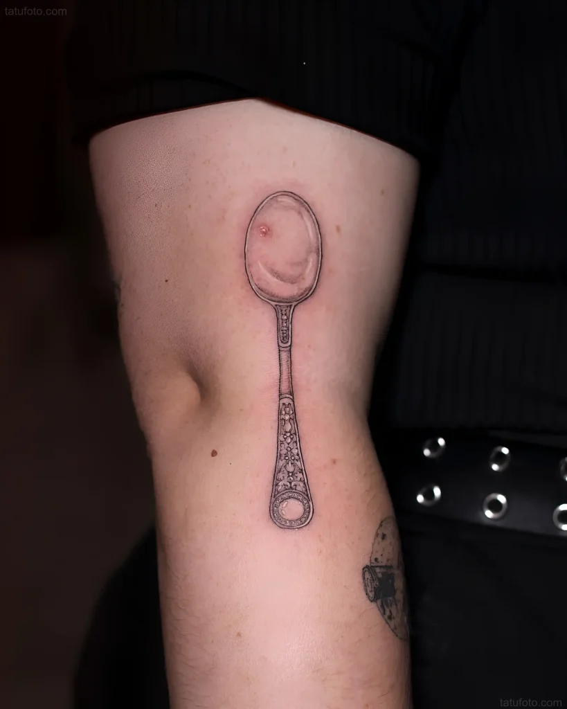 Schwarz-weißes Löffel-Tattoo an der Innenseite des Unterarms, im Grafikstil mit detaillierter Musterzeichnung am Griff.