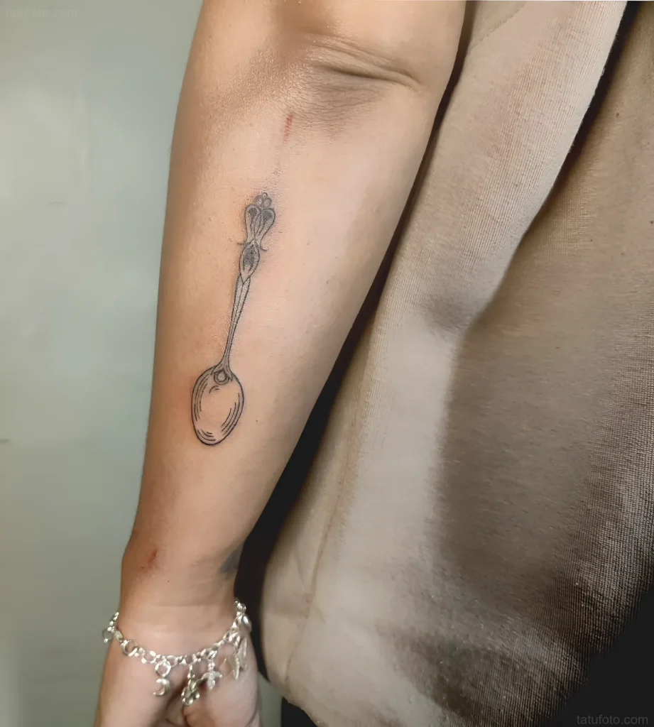 Minimalistisches Löffel-Tattoo an der Innenseite des Unterarms, im Linienkunststil.