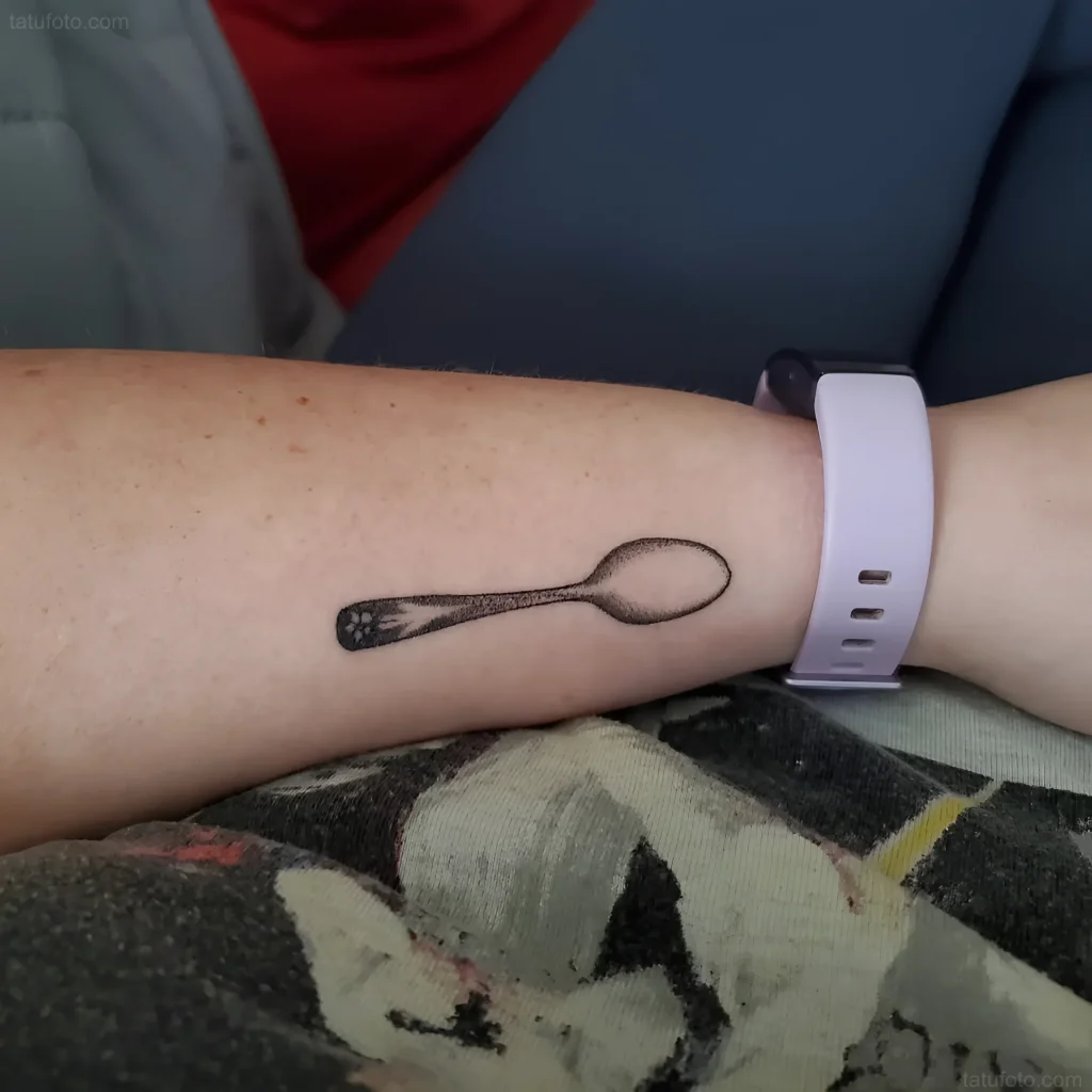Minimalistisches Löffel-Tattoo am Arm, im Dotwork-Stil, mit einer Katzenpfote im Löffel.