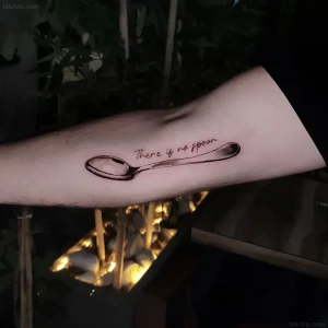 Черно-белая татуировка ложки на предплечье с фразой 'There is no spoon' - символ принятия реальности и отказа от иллюзий.
