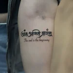 Минималистичная татуировка с фразой 'The end is the beginning' на санскрите (деванагари) черными чернилами на бицепсе