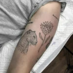 Черно-белая татуировка на бедре с изображением головы леопарда и цветка протея, выполненная в технике графики.
