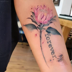 Фото татуировки цветка протея в акварельной технике на руке, с надписью 'forever' и изображением пчелы.