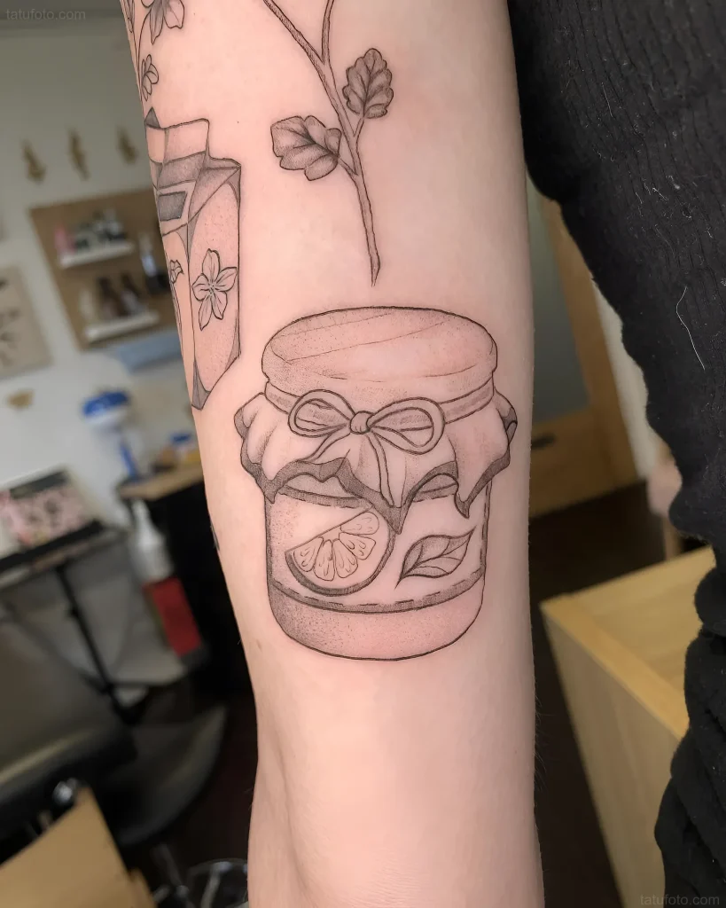 手臂上的纹身草图：一个带有柑橘片和丝带的果酱罐，以及一枝点刺风格的花朵。
