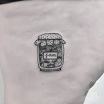 Минималистичная татуировка банки с клубничным вареньем на боку, выполненная в технике лайнарт.