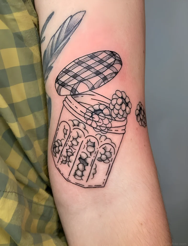 手臂上的黑白纹身，描绘了一个装满浆果的打开的果酱罐，采用老式风格。